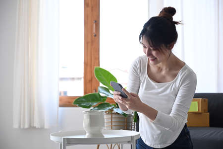 Young female online seller using smartphone taking photo of product for upload to website online...