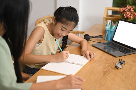 Happy asian girl doing assignments with her mother in home kitchen.の写真素材