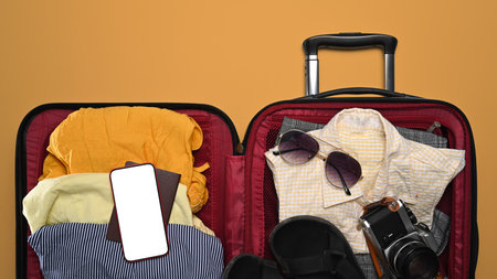 Open suitcase, smart phone, sunglasses, camera and passport on yellow background for summer...