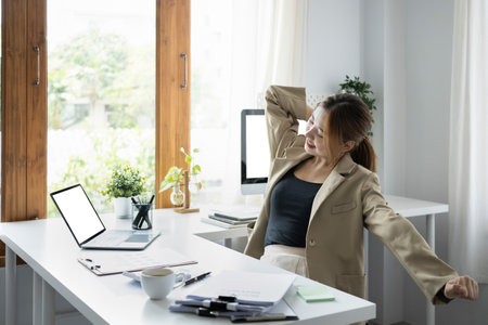 Young female employee stretching arms, relaxing from work in office.の写真素材
