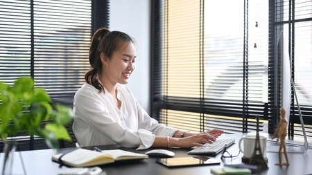 Successful asian woman entrepreneur sitting in bright modern office and working with computer.の写真素材