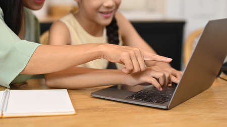 Cropped shot mother helping her daughter doing homework, having online class on computer laptop at...