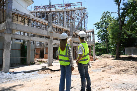 Rear view civil engineer team wearing yellow vests is discussing the construction process together...