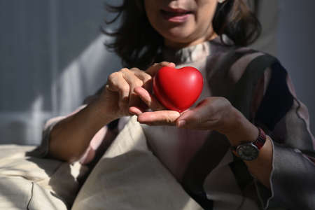 Smiling middle aged woman holding heart shape. Elderly care, insurance, heart health and quality of life for elderly concept.の写真素材
