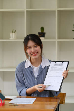 Confident female financial advisor holding contract and smiling at camera. Real estate investors,...