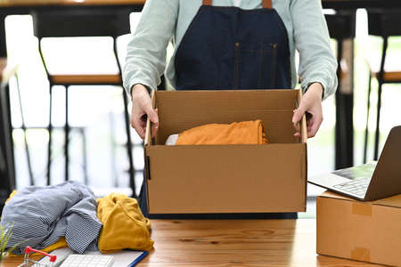 Cropped shot small business owner wearing apron holding cardboard in her hands. Online selling,...