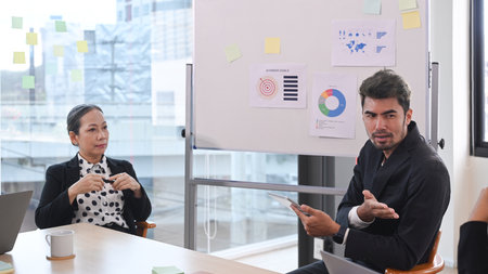 Handsome young businessman sharing creative ideas, explaining strategy to diverse business people at...