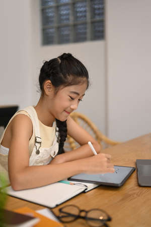 Smiling Asian girl doing homework on digital tablet, studying through online learning system.の写真素材