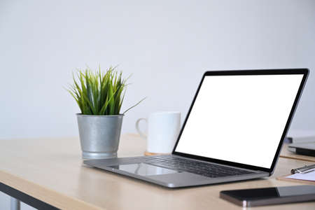 Laptop computer, smart phone, houseplant and coffee cup on wooden desk. Modern workplace.
