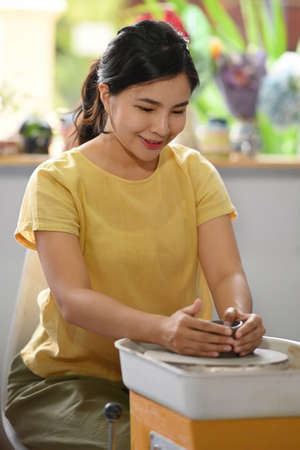 Concentrated woman is creating handmade tableware in pottery workshop. Pottery working, handmade clay products and creative skills.の写真素材