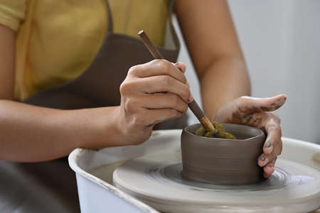 Cropped shot ceramicist hands shaping ceramic bowl on pottery wheel in ceramics studio. Pottery working, handmade clay products and creative skills.の写真素材