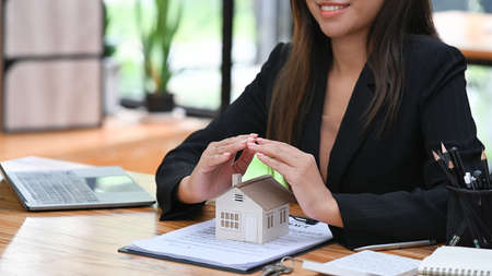 Female real estate agent hands sheltering house model. Real estate investment, property insurance and security concepts.の写真素材