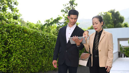 Mature businesswoman and young businessman talking each other and walking outside modern office building.の写真素材