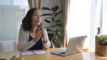 Mature woman resting and drinking hot coffee during remote working from home.の写真素材