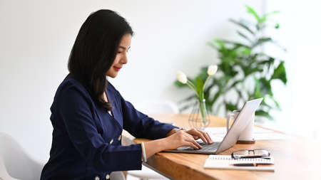 Beautiful young female manager sitting at her spacious office and using laptop computer.の写真素材