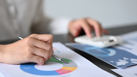 Professional businesswoman checking financial reports and using calculator to compute and summarize...