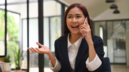 Happy beautiful young business woman having negotiations with business partner on cell phone.の写真素材