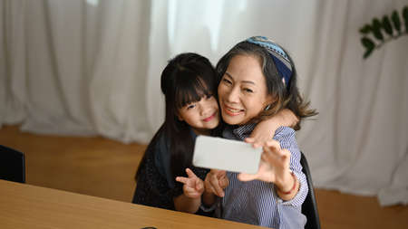 Happy grandmother and cute granddaughter having fun taking selfie on smart phone. Happy moment, multi generational, family, love concept.の写真素材