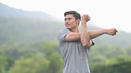 Young asian man in sportswear stretching his arm, warming up before morning workout at outdoors....