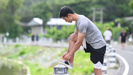 Athletic man tying shoelaces before running, getting ready for jogging outdoors. Healthy lifestyle,...