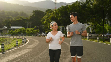 Active mature woman and her personal trainer jogging at the park in evening. Healthy lifestyle and fitness concept.の写真素材