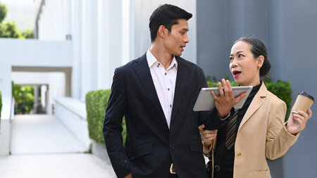 Friendly senior female manager discussing online information with young businessman while walking...