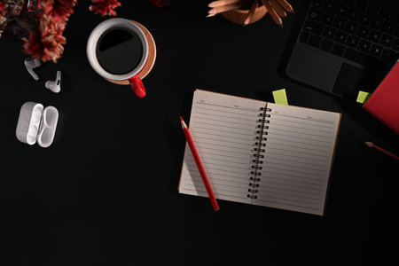 Flat lay blank notepad, wireless earphone and coffee cup on black background.