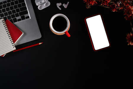 Modern workspace with smart phone, laptop, coffee cup and notepad on black background. Flat lay, top...