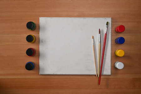 Flat lay blank canvas, watercolors and paint brushes on wooden background. Artist or designer workplace.の写真素材