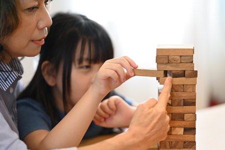 Joyful little asian child and grandmother playing wood block stacking board game, spending leisure weekend at home together at home.の写真素材