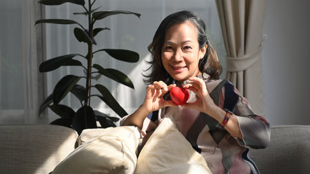 Happy middle aged woman holding heart shape. Elderly care, insurance, heart health and quality of life for elderly concept.の写真素材