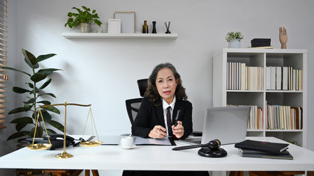 Elegant mature female lawyer in judge uniform sitting at personal office. Lawyer, justice and law and attorney concept.の写真素材