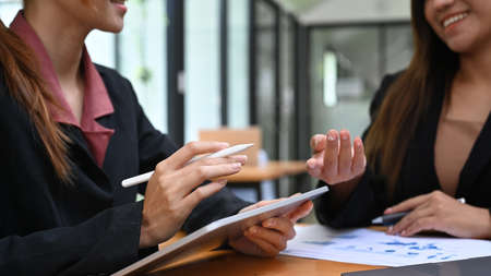 Cropped view of two young businesswomen analyzing and discussing financial graph, charts and diagrams together.の写真素材