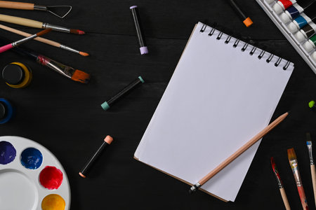 Sketchbook, paint brushes, tube paint, watercolor and palette on black wooden table. Artist workspace, Art, workshop, painting, creativity concept.の写真素材