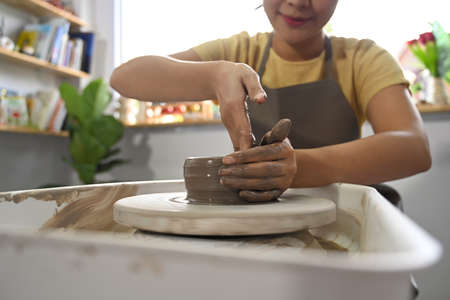 Woman in apron creating handicraft crockery on the pottery wheel in workshop. Activity, handicraft, hobbies concept.の写真素材