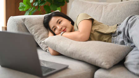 Happy asian woman lying on comfortable sofa and watching movie on laptop computer.の写真素材