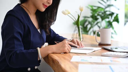 Concentrated female accountant taking notes on notebook and working with financial document.の写真素材