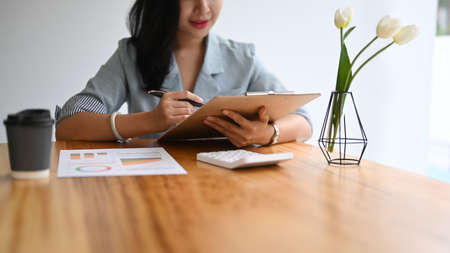 Young female investor sitting in personal office and reading business plan on clipboard.の写真素材