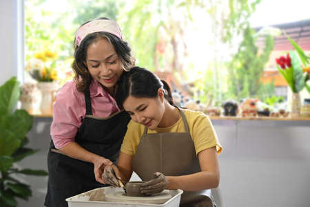 Mature woman potter teaching young woman sculpting clay dishes in workshop. Activity, handicraft,...