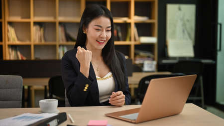 Happy asian business woman looking at laptop, received great news and celebrating her success.