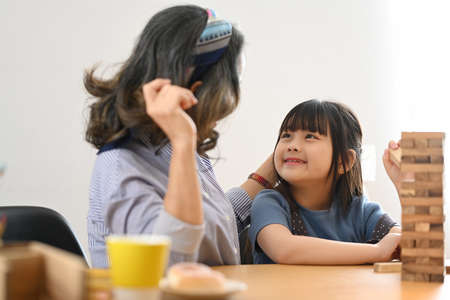 Little asian child and middle aged grandma enjoy playing wood blocks tower game in bright living room.の写真素材