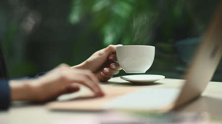 Cropped image of young woman hand holding cup of hot coffee with natural morning background.の写真素材