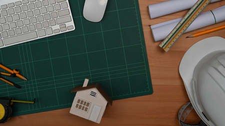 From above view Engineer or Architect workspace with laptop, blueprints, house model and hardhat on...