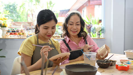 Happy mature woman and young woman painting pottery bowl in handicraft workshop.の写真素材