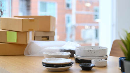 Set of ceramic products and parcel boxes on wooden table in modern home office. E-commerce, Online...