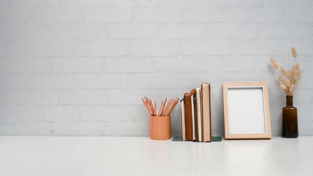 Home office desk with blank picture frame, books and pencil holder on white table. Copy space for advertise text.の写真素材