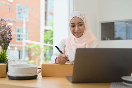 Muslim businesswoman looking at laptop screen for checking order on internet. Online selling, E-commerce concept.の写真素材