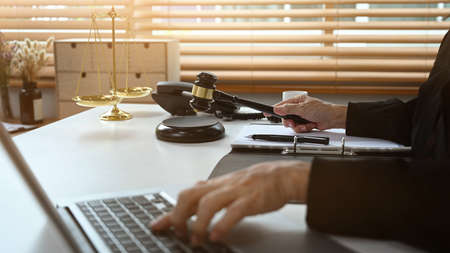 Cropped shot of senior female judge working on laptop computer, online legal advice.