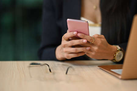 Cropped view of working woman using mobile phone, communicating in social media.