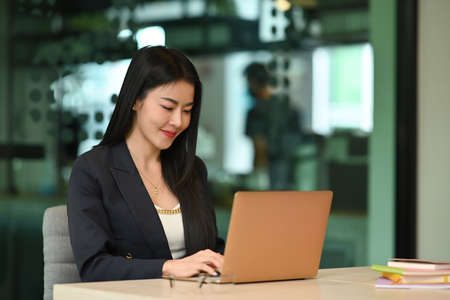 Millennial female entrepreneur using laptop, working on research project in her personal office.の写真素材